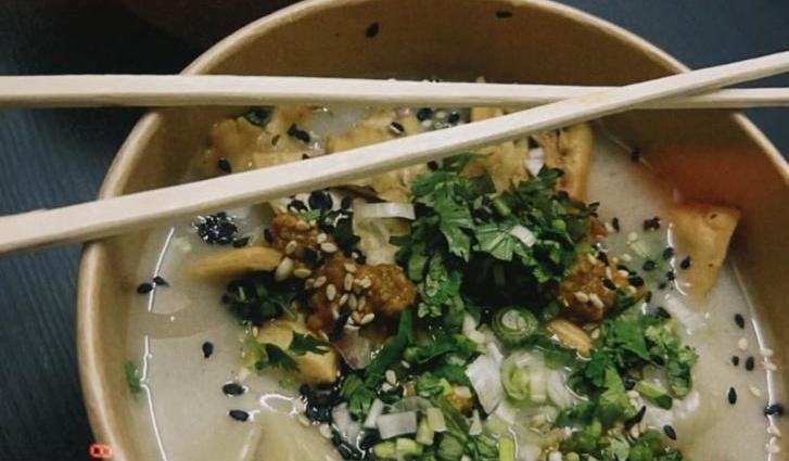 A bowl of momos in broth with chopsticks resting across it