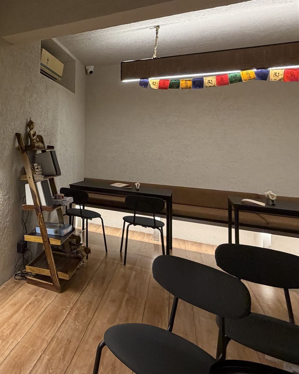 Café seating with prayer flags above a long table, black chairs and a Buddha on a wooden shelf