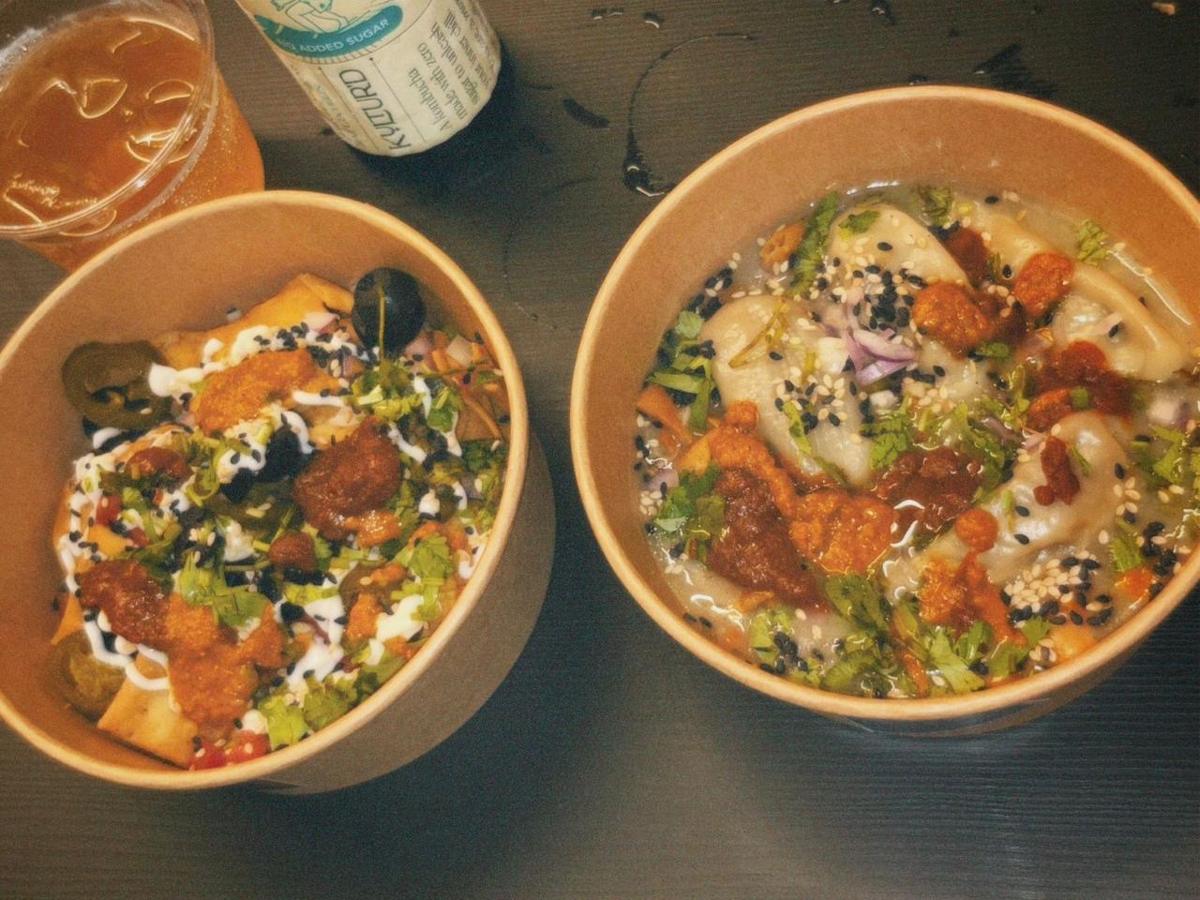 Two kraft bowls of momos with toppings, kombucha alongside